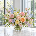 Pastel peach and pink wedding arrangement with lavender and light blue garden flowers in clear glass bowl by a large window