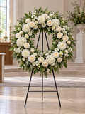 Peaceful Tribute Wreath, circular white and ivory floral sympathy wreath with visible central opening and complete black standing easel in serene chapel